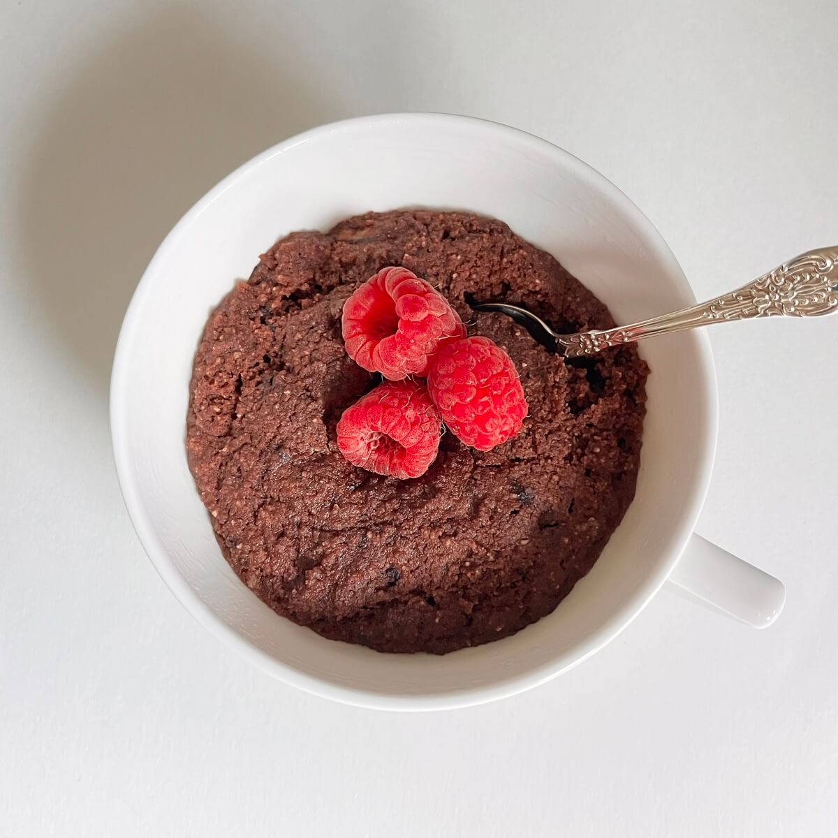 A mug cake with three raspberries on top.