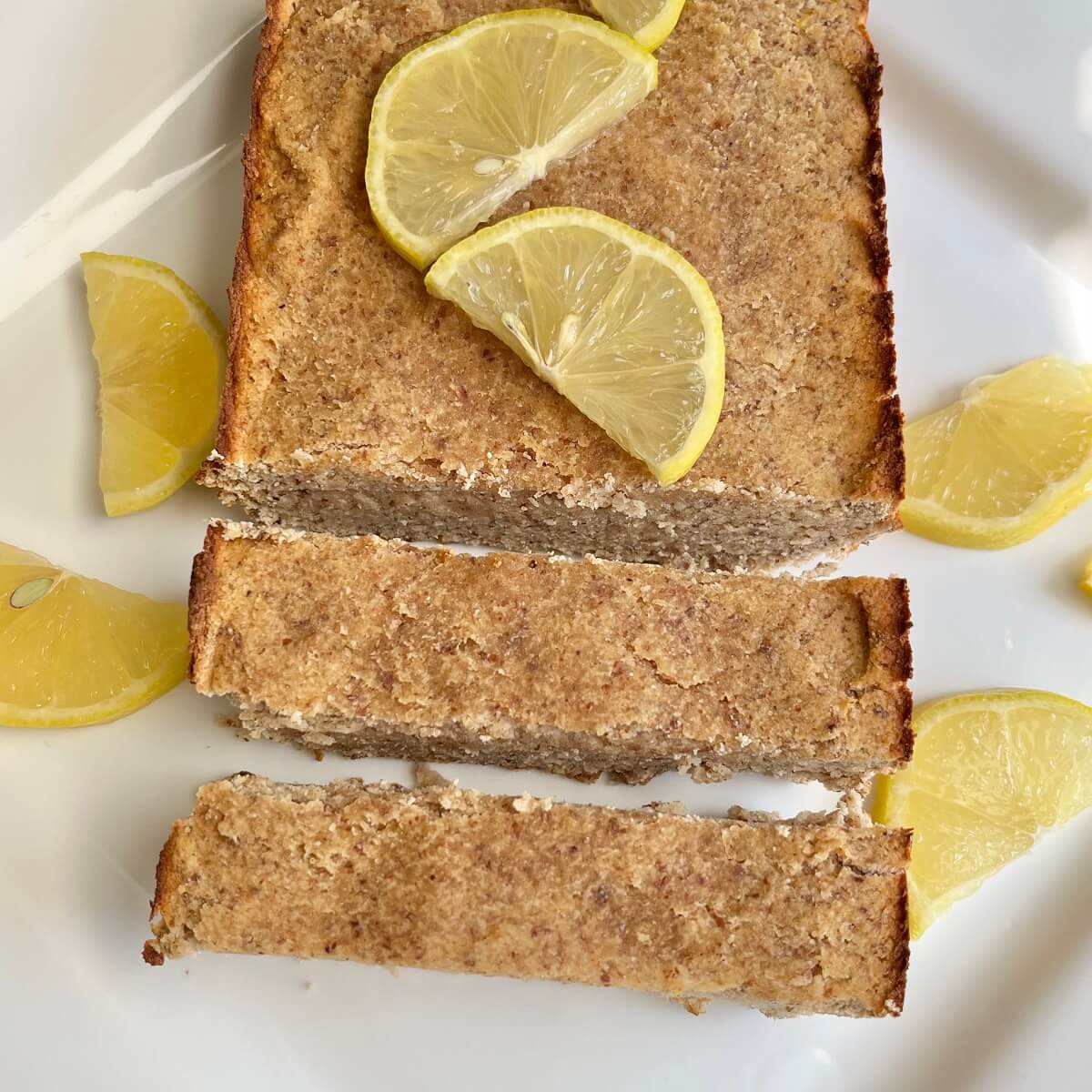 A loaf of paleo lemon cake with two thick slices cut.
