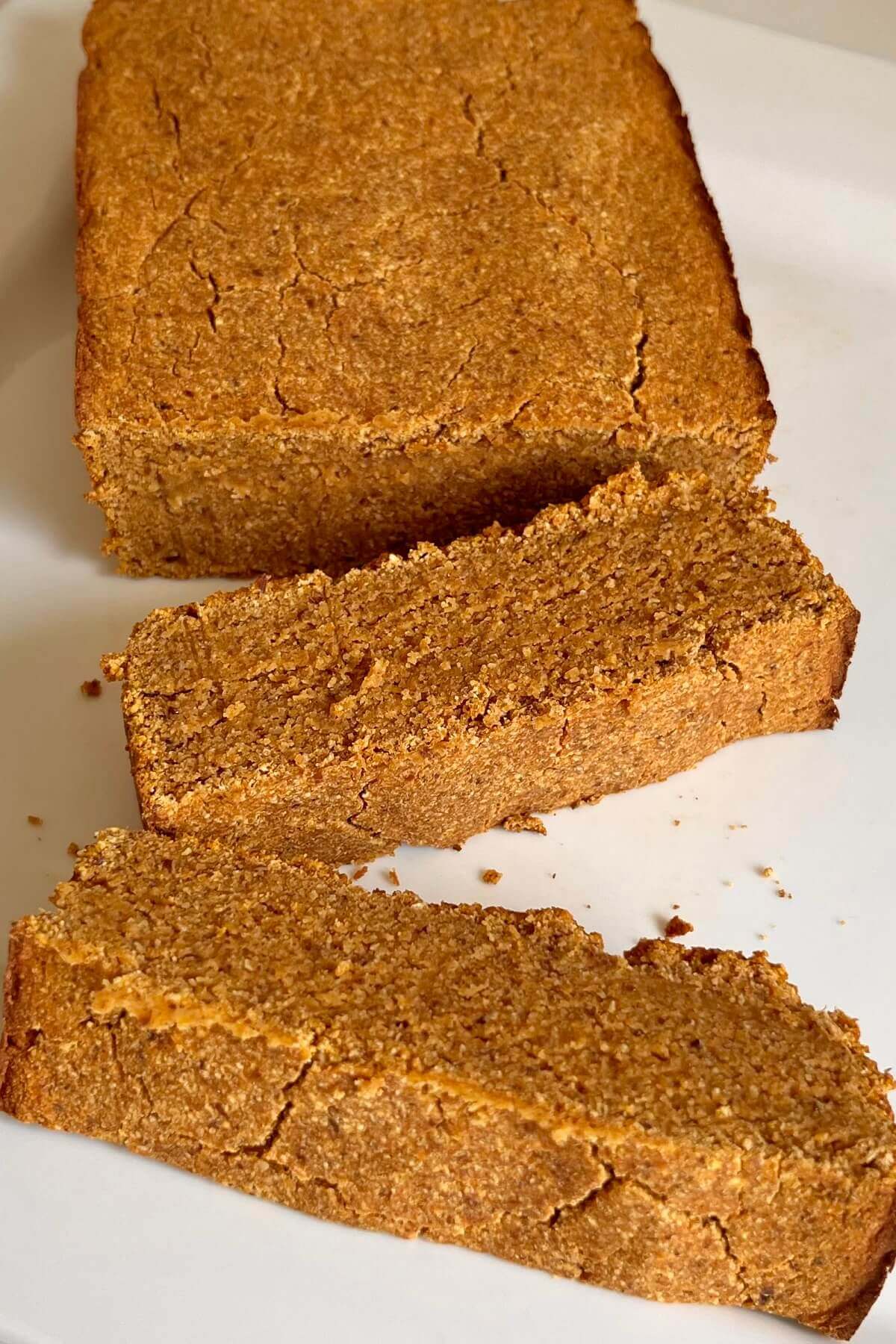 A loaf of paleo pumpkin bread on a white platter with two slices cut.