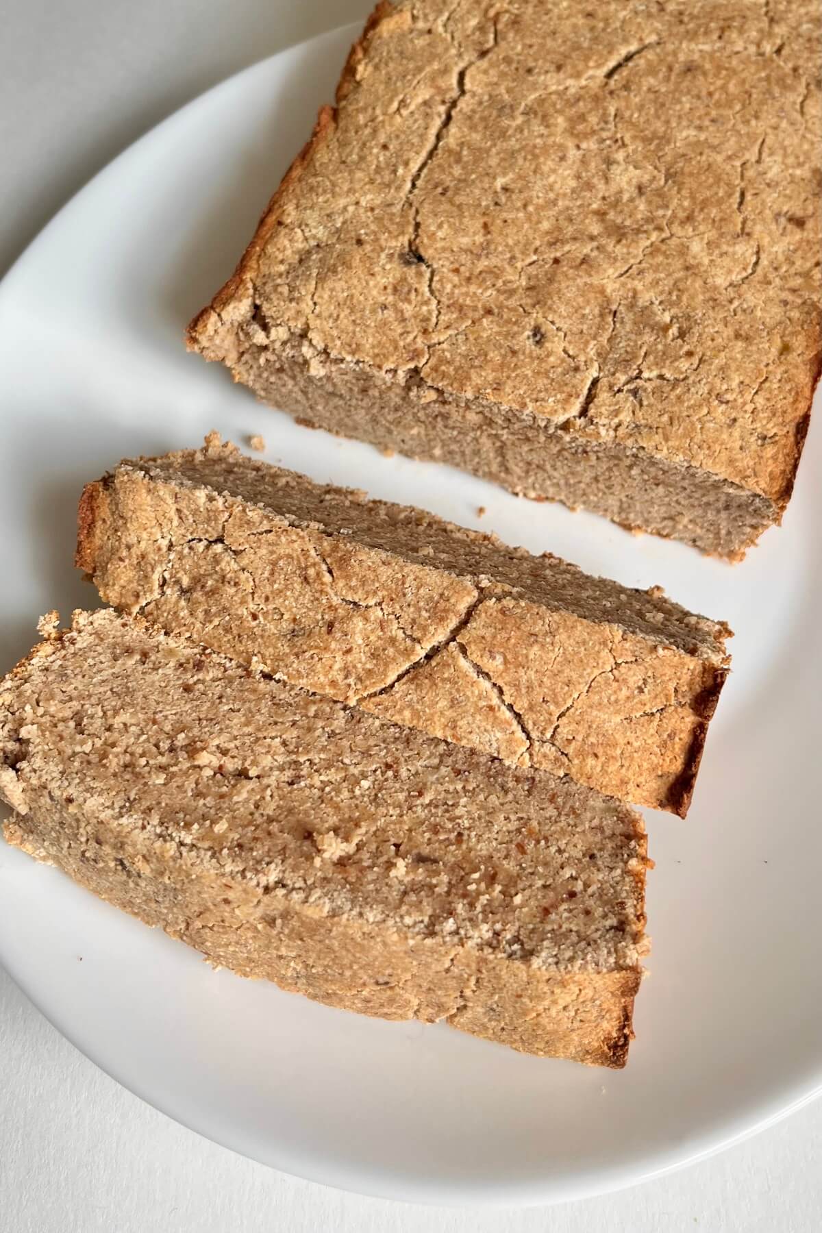 A loaf of paleo banana bread on a white plate with two slices cut.