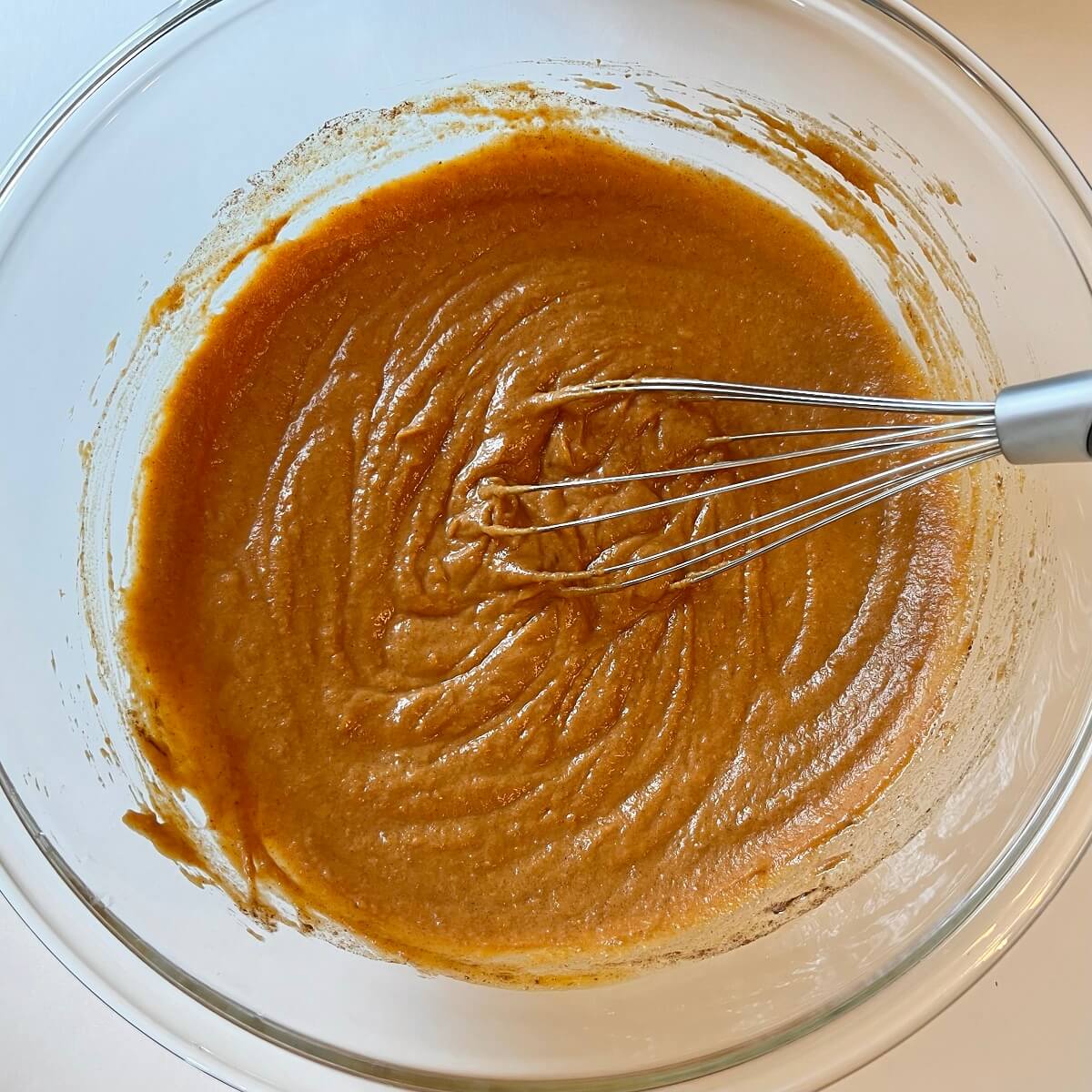 Wet ingredients for pumpkin bread in a glass mixing bowl.
