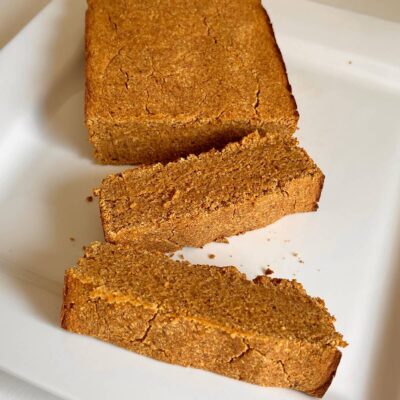 A loaf of coconut flour pumpkin bread on a white plate with two thick slices cut.