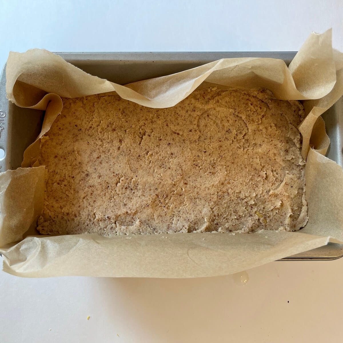 Raw lemon cake in a loaf pan lined with parchment paper.