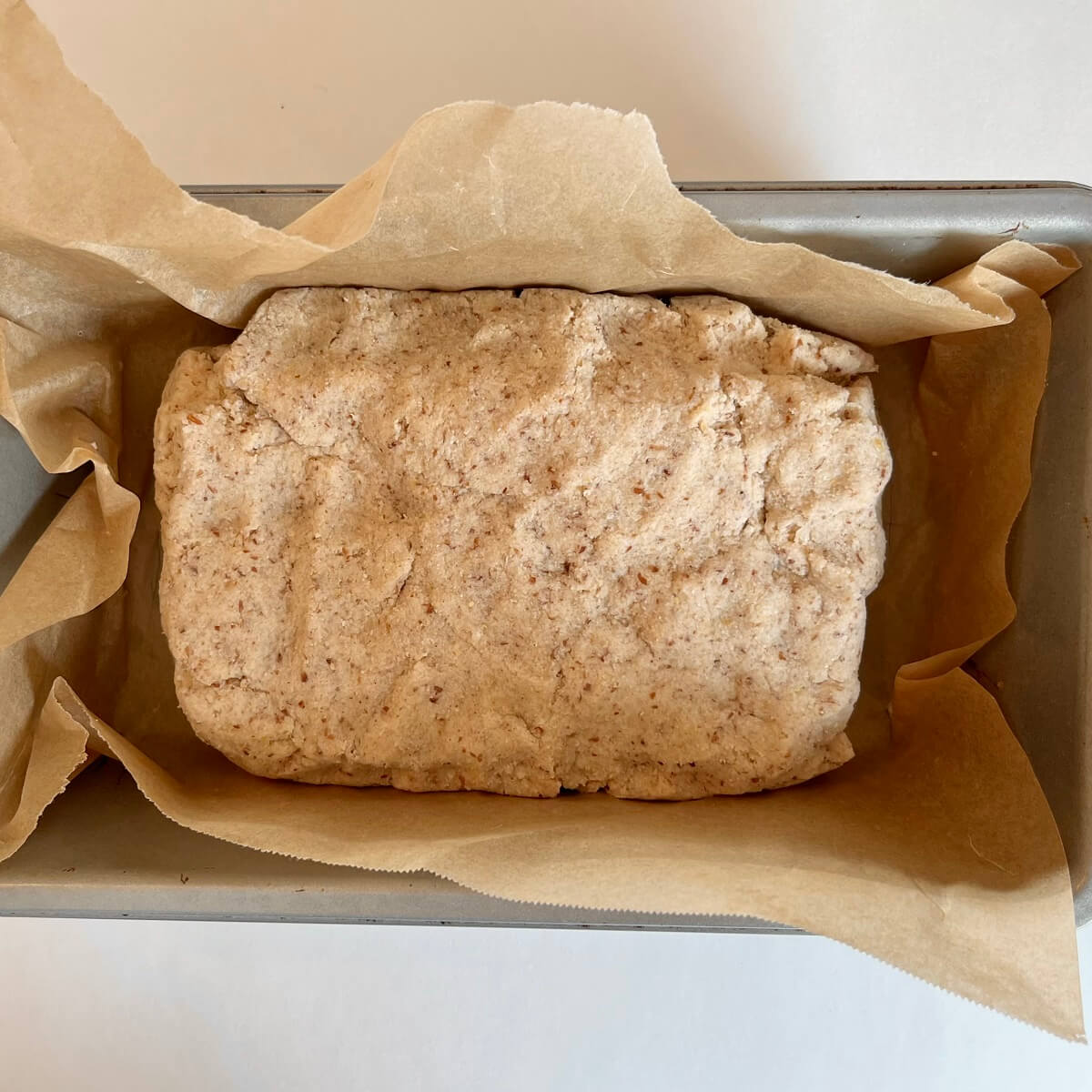 Raw bread dough in a metal loaf pan lined with parchment paper.