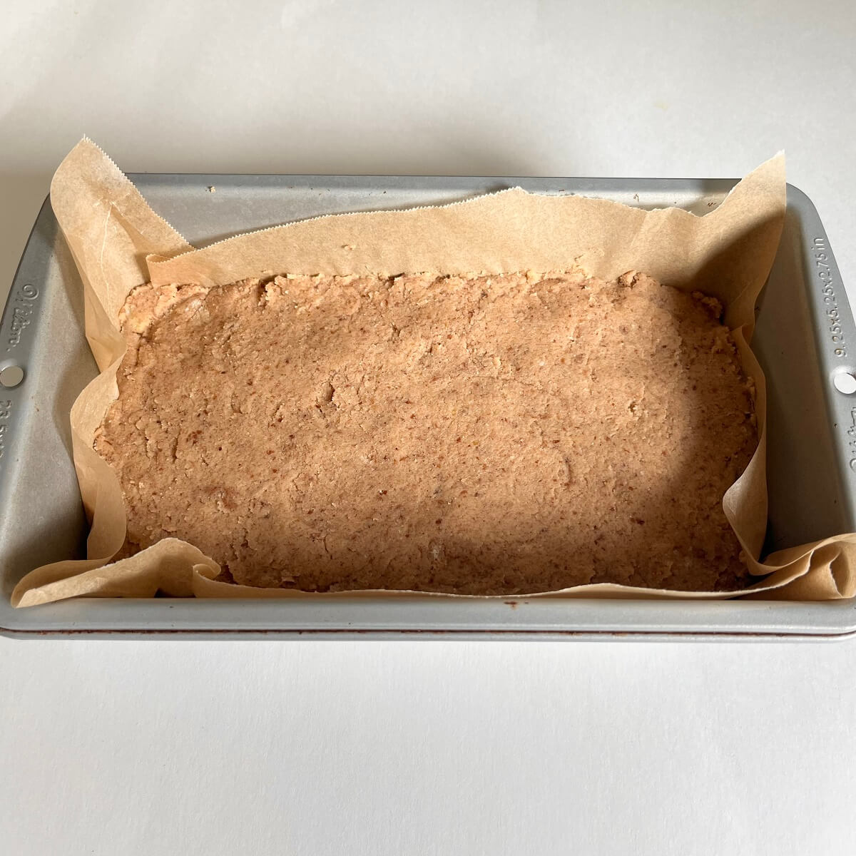 Raw paleo banana bread in a metal loaf pan lined with parchment paper.