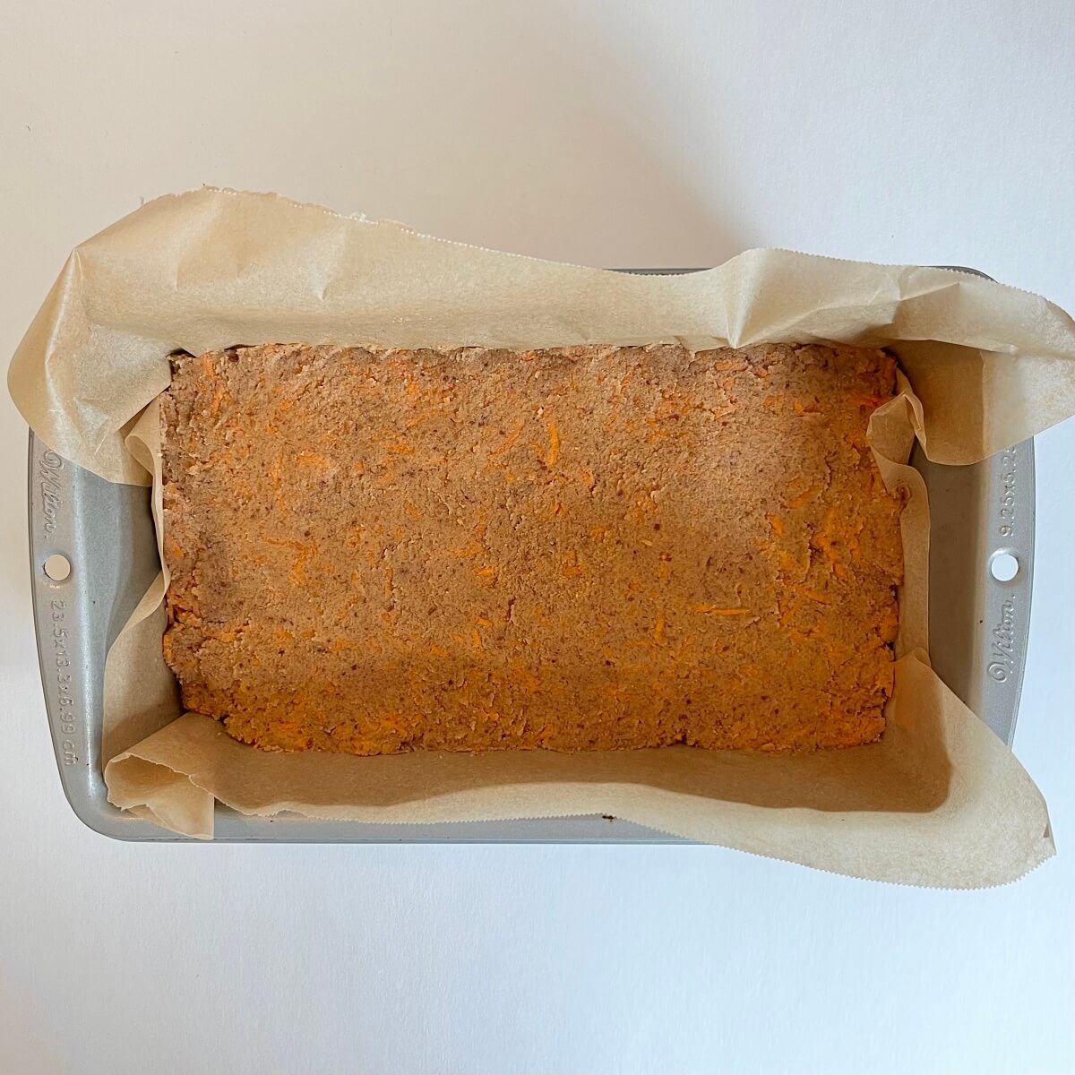 Raw carrot cake in a loaf pan lined with parchment paper.