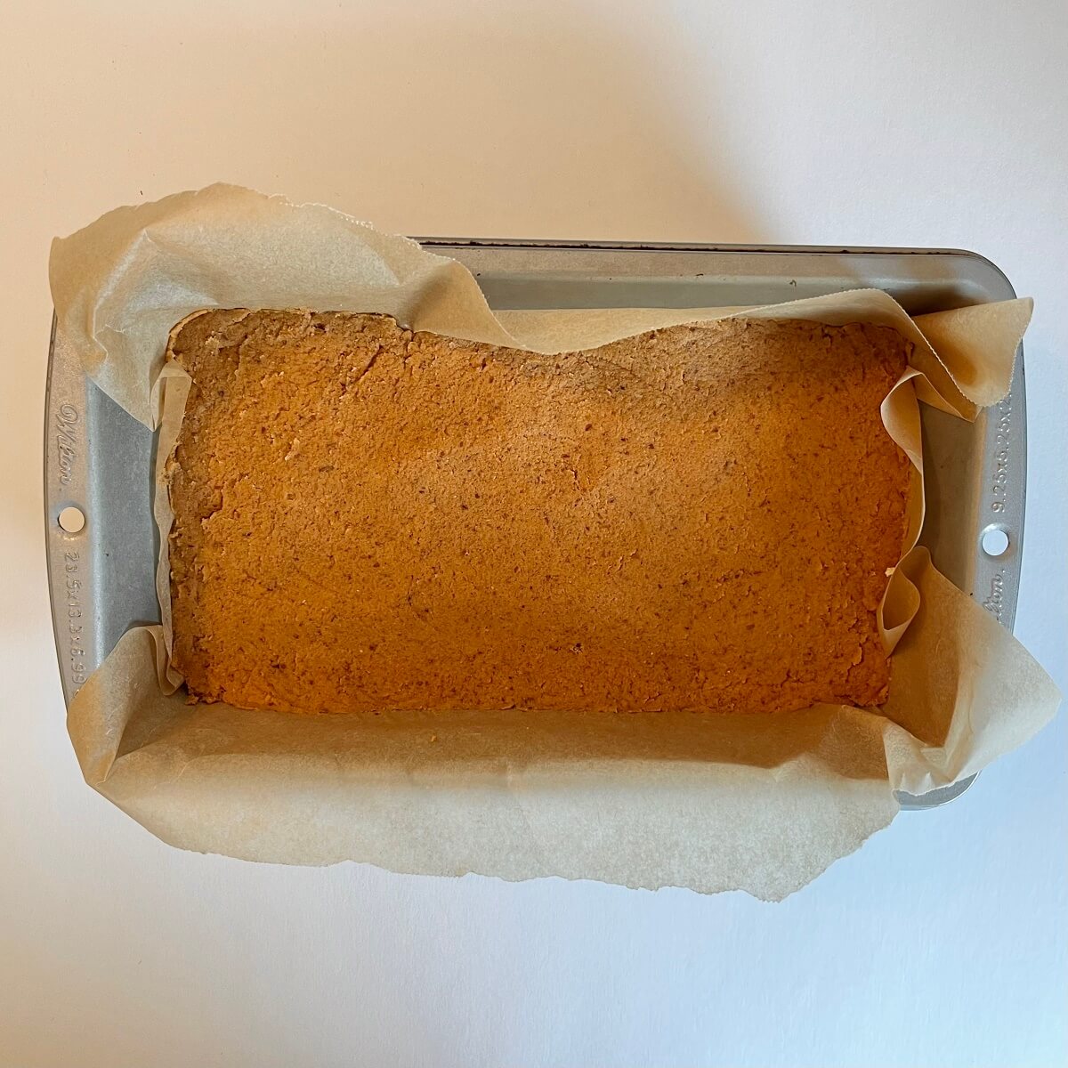 Raw pumpkin bread in a metal loaf pan lined with parchment paper.
