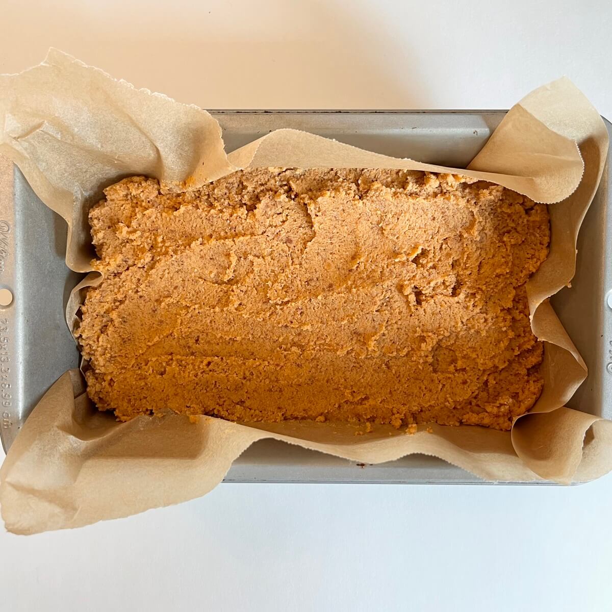 Raw sweet potato bread in a loaf pan lined with parchment paper.