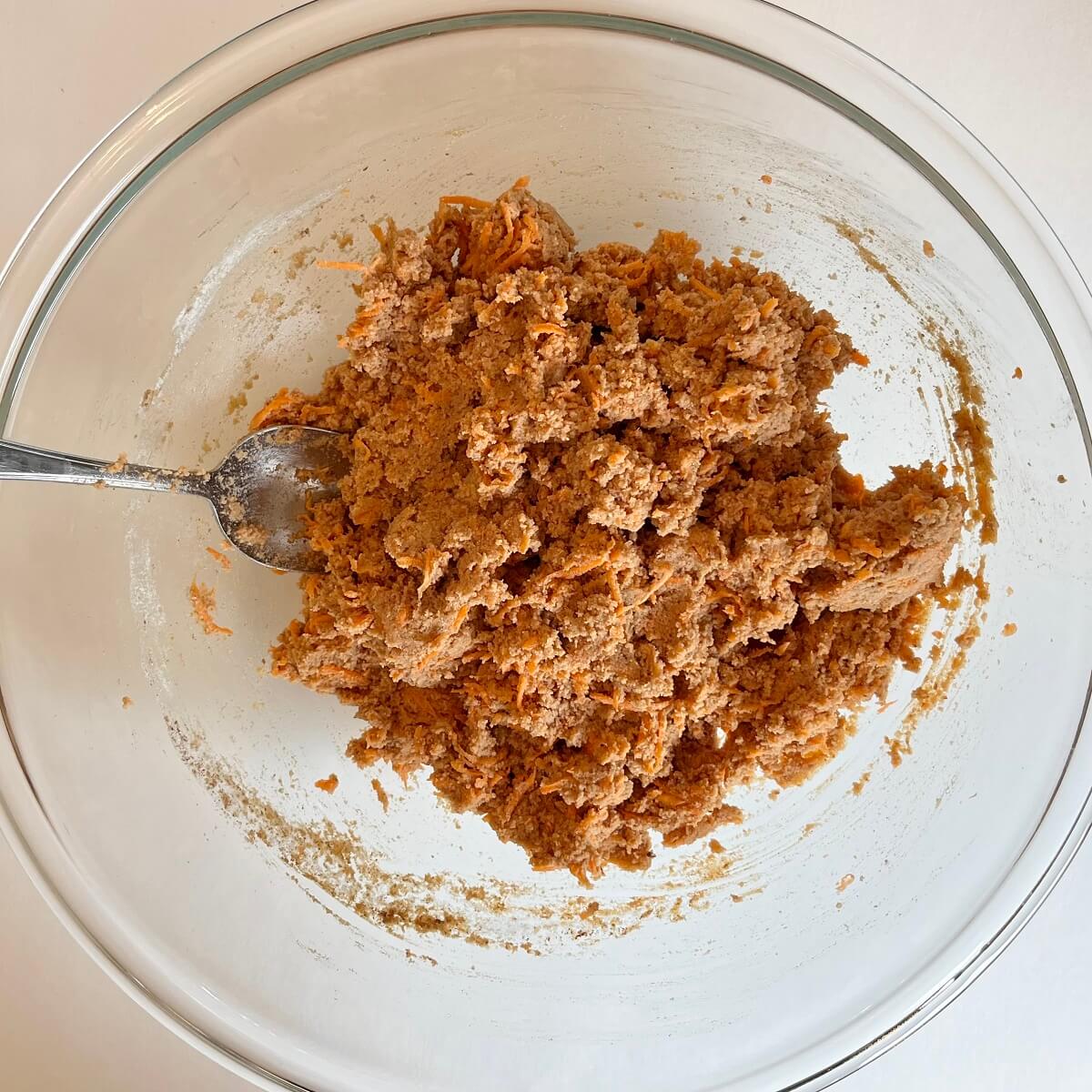 Thick carrot cake batter in a bowl with a spoon.