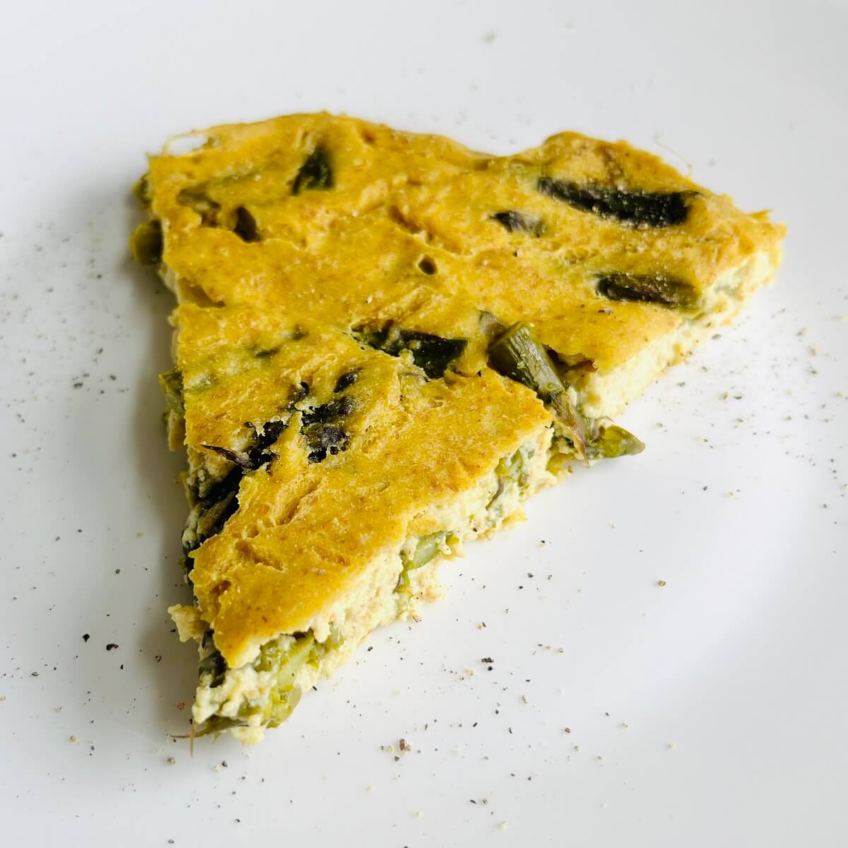 A slice of vegan asparagus frittata on a white plate.