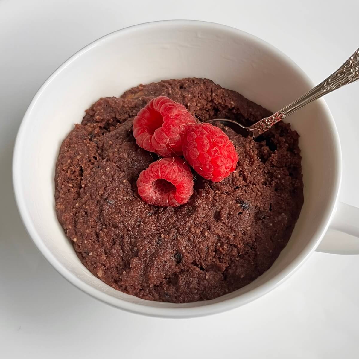 Cake in a mug with raspberries on top.