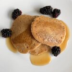 Three vegan oat flour pancakes with blackberries and maple syrup.