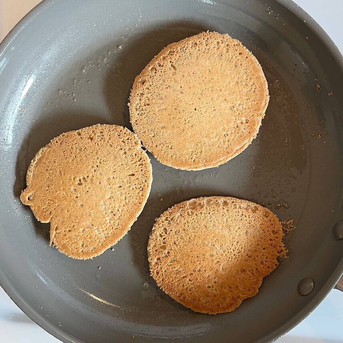 Vegan oat pancakes cooking in a pan.