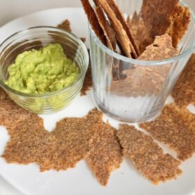 A crackers next to a glass bowl of guacamole.