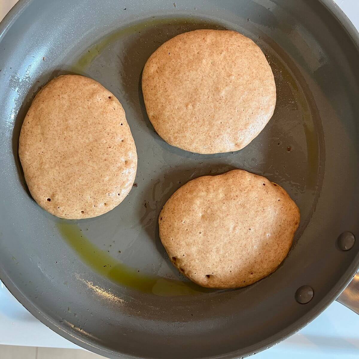 Pancakes ready to be flipped in a nonstick frying pan.