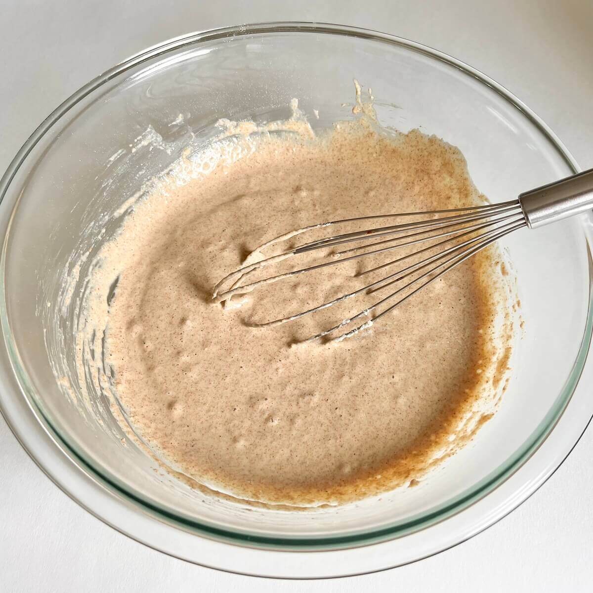 Thick pancake batter being stirred with a whisk in a glass mixing bowl.