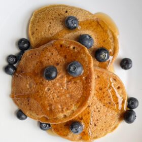 Pancakes drizzled with maple syrup with blueberries scattered on top.