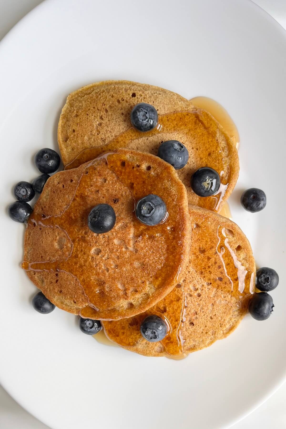 Three pancakes on a white plate with blueberries and syrup.