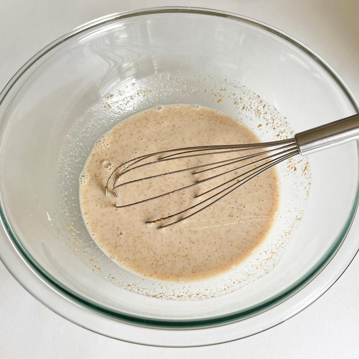 Wet ingredients for pancakes in a large glass mixing bowl with a whisk.