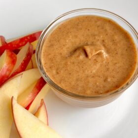 A dish of caramel sauce next to some sliced apples.