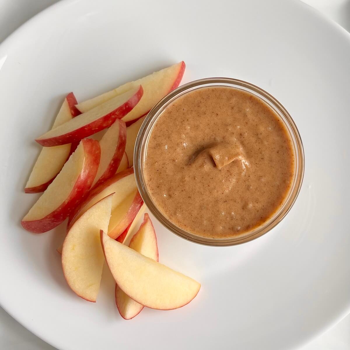 A dish of vegan date caramel sauce next to some sliced apples.