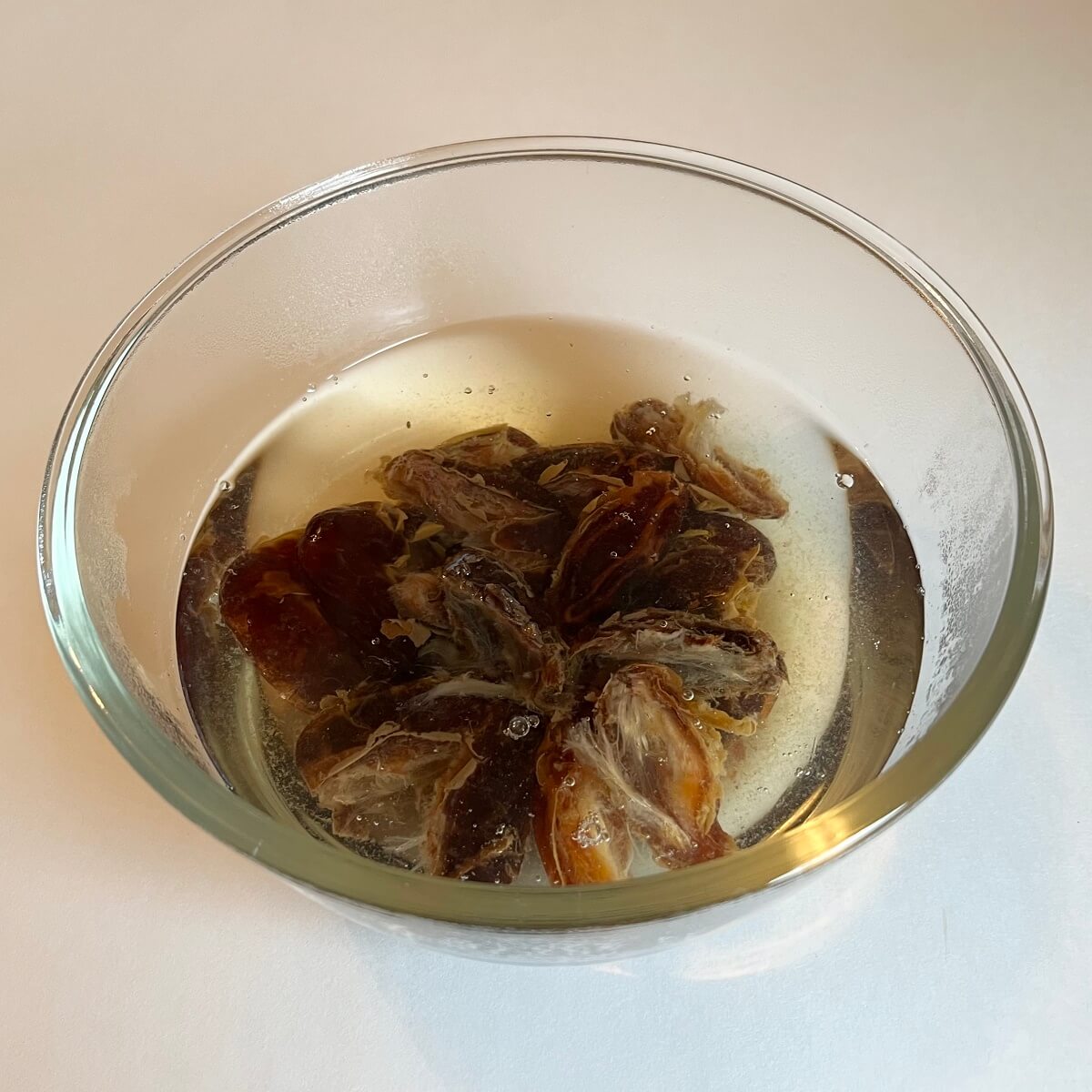 Dates being soaked in boiling water in a glass bowl.