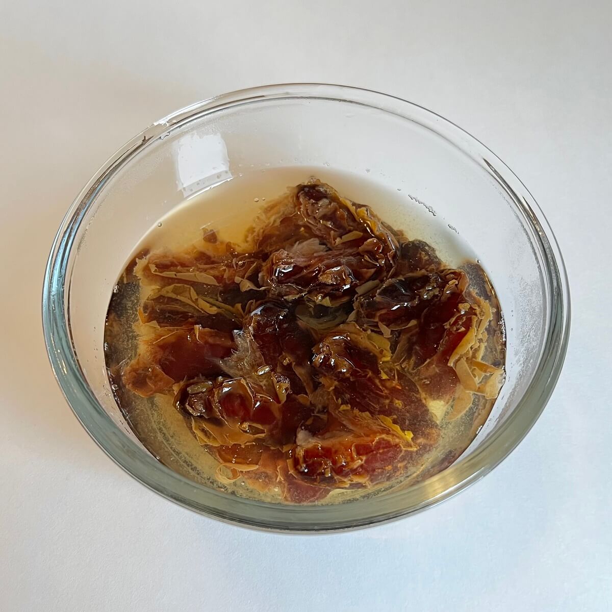 Medjool dates soaking in hot water in a glass bowl.