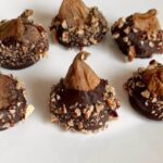 Chocolate covered figs sprinkled with chopped pecans on a white plate.