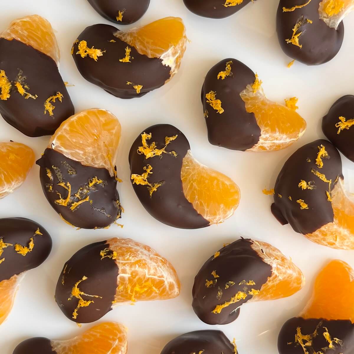Chocolate covered orange segments sprinkled with orange zest on a white plate.