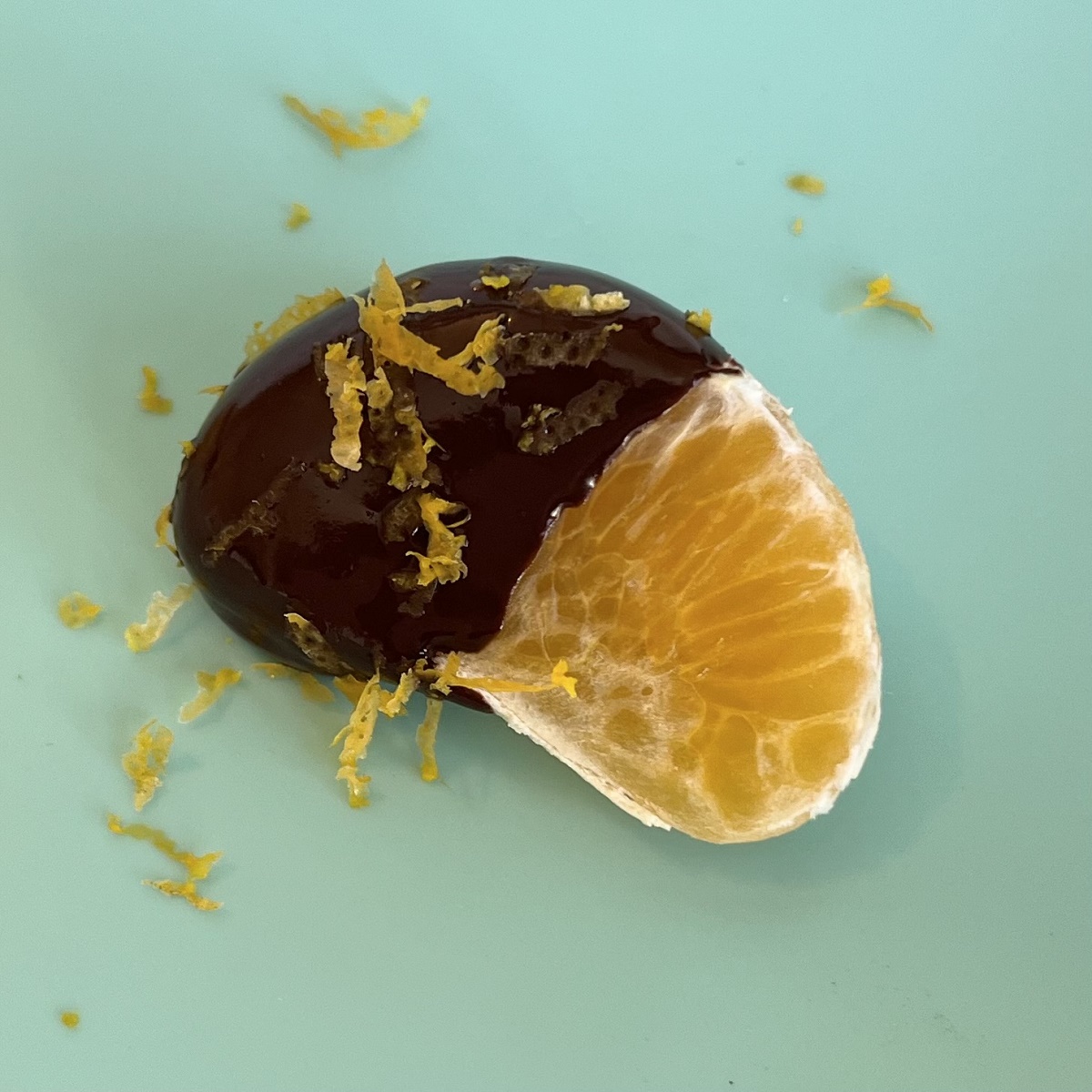A single chocolate dipped clementine segment on a turquoise silicone baking mat.