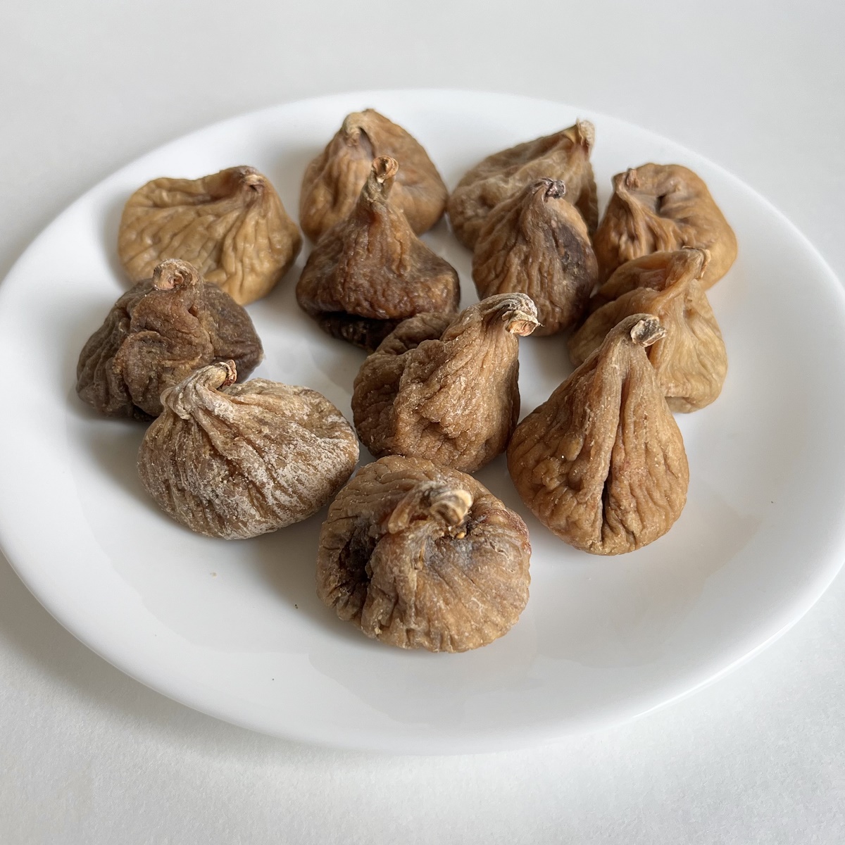Twelve dried figs on a white plate.