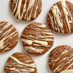 Light brown cookies drizzled with white chocolate on a white platter.
