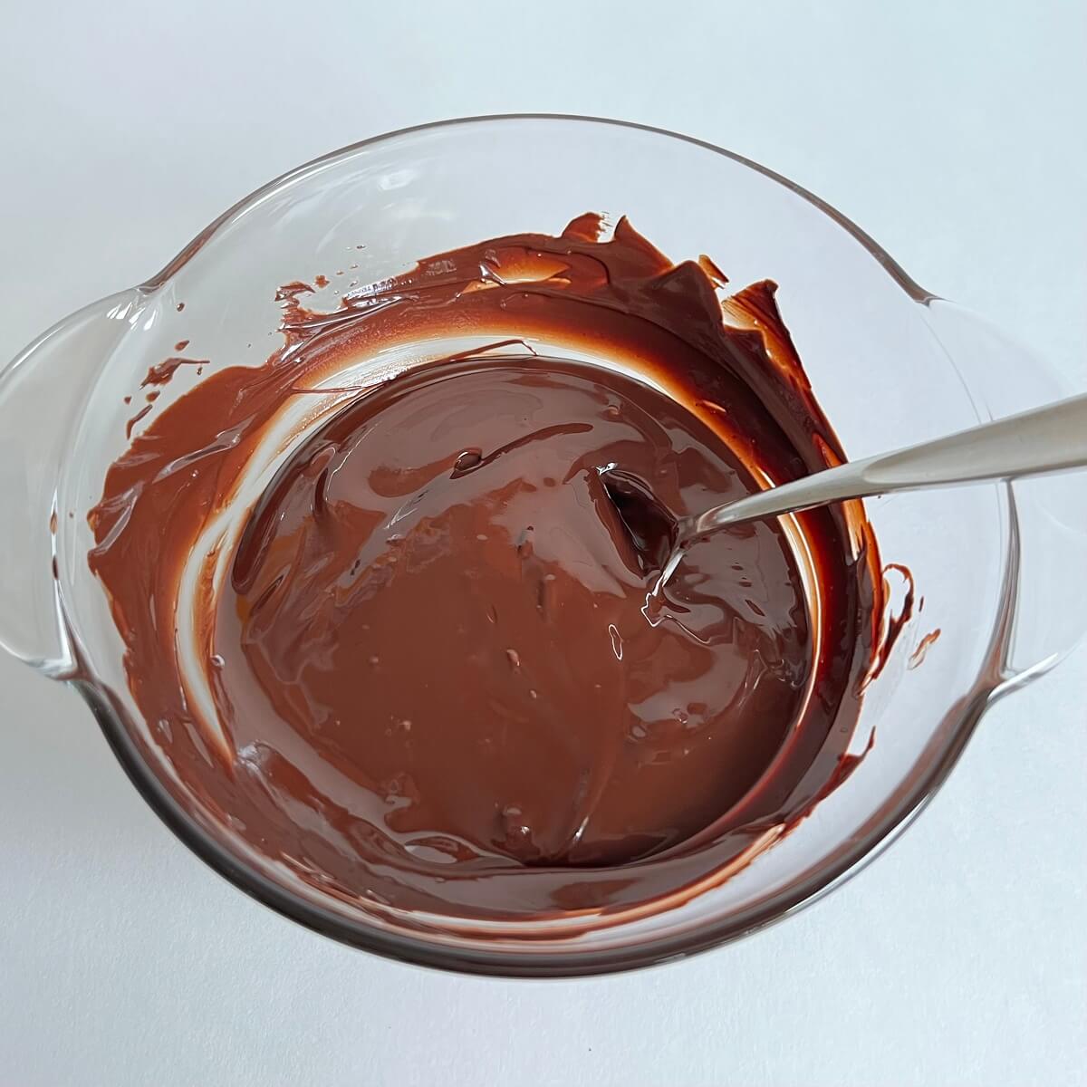 Hot melted chocolate in a glass bowl with a stainless steel spoon.