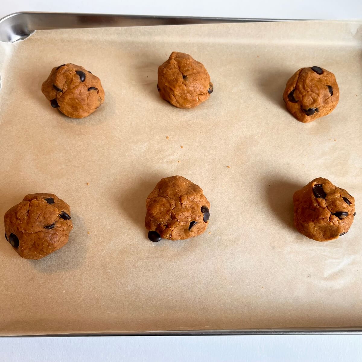 Pumpkin cookie dough balls on a parchment paper lined sheet pan.