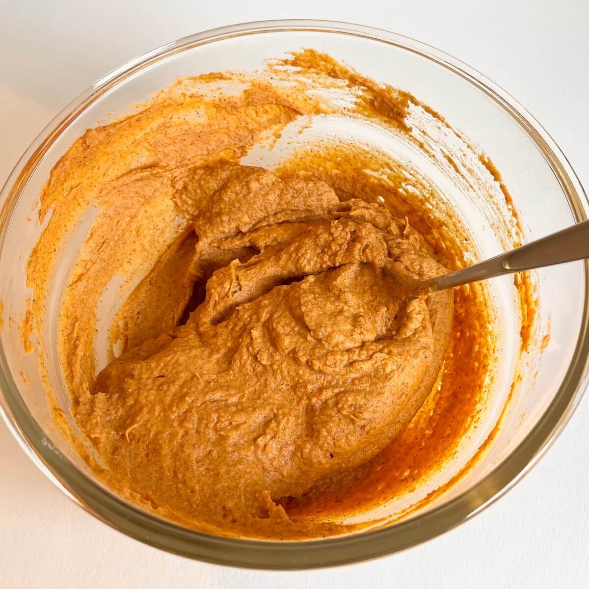 Pumpkin, almond butter, and vanilla extract stirred in a glass mixing bowl.