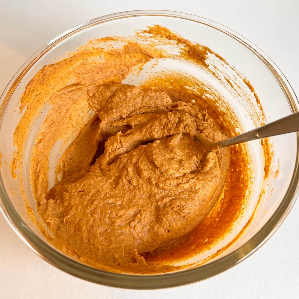 Pumpkin, almond butter, and vanilla extract stirred in a glass mixing bowl.