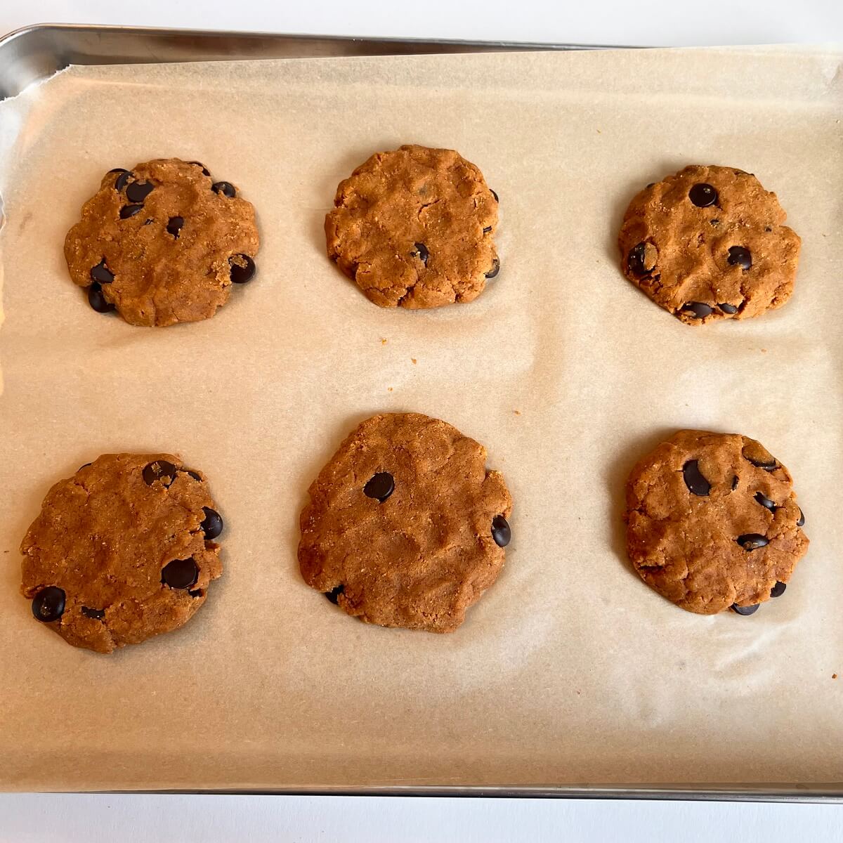 Raw chocolate chip pumpkin cookies on a sheet pan lined with parchment paper.