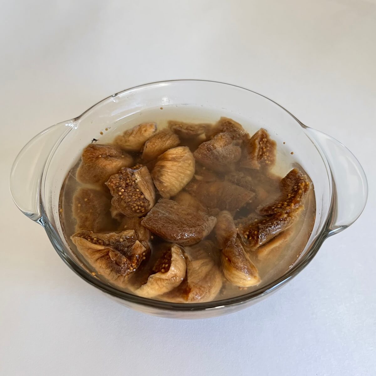 Chopped figs soaking in water in a glass bowl.