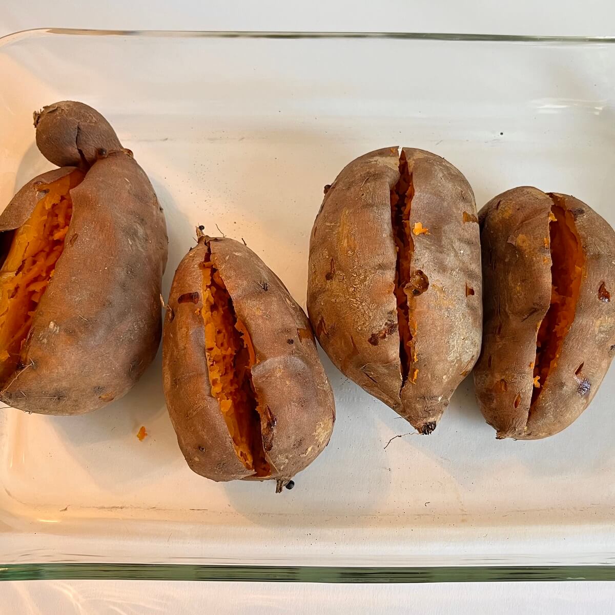 Four baked sweet potatoes in a glass baking dish.