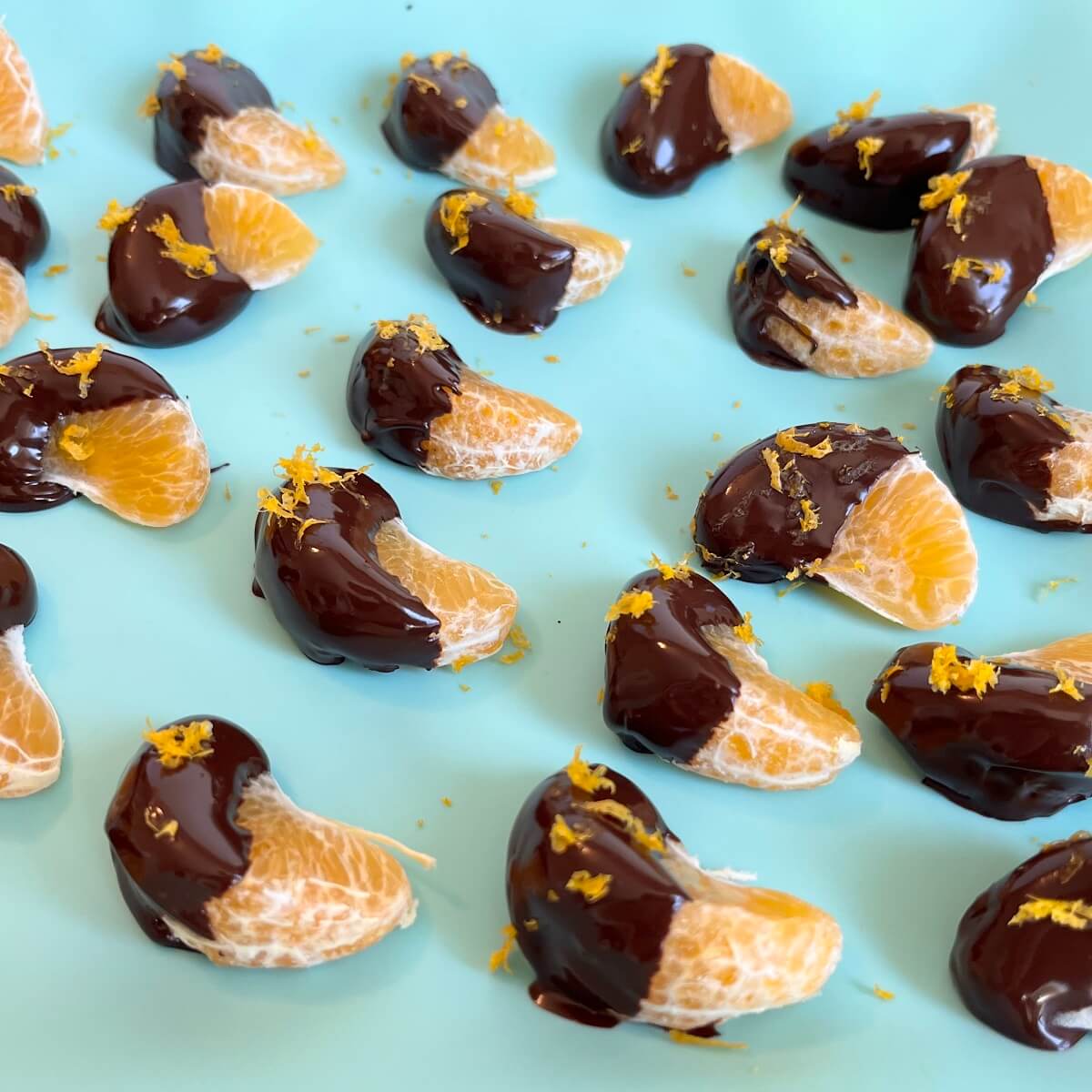 Clementine segments dipped in melted chocolate on a silicone baking mat.