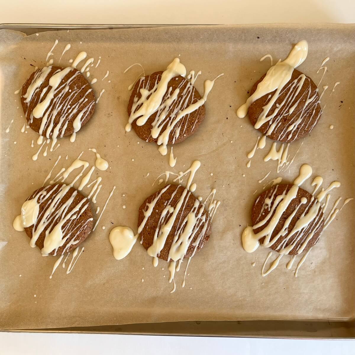 Cookies drizzled with dairy-free white chocolate on a sheet pan.