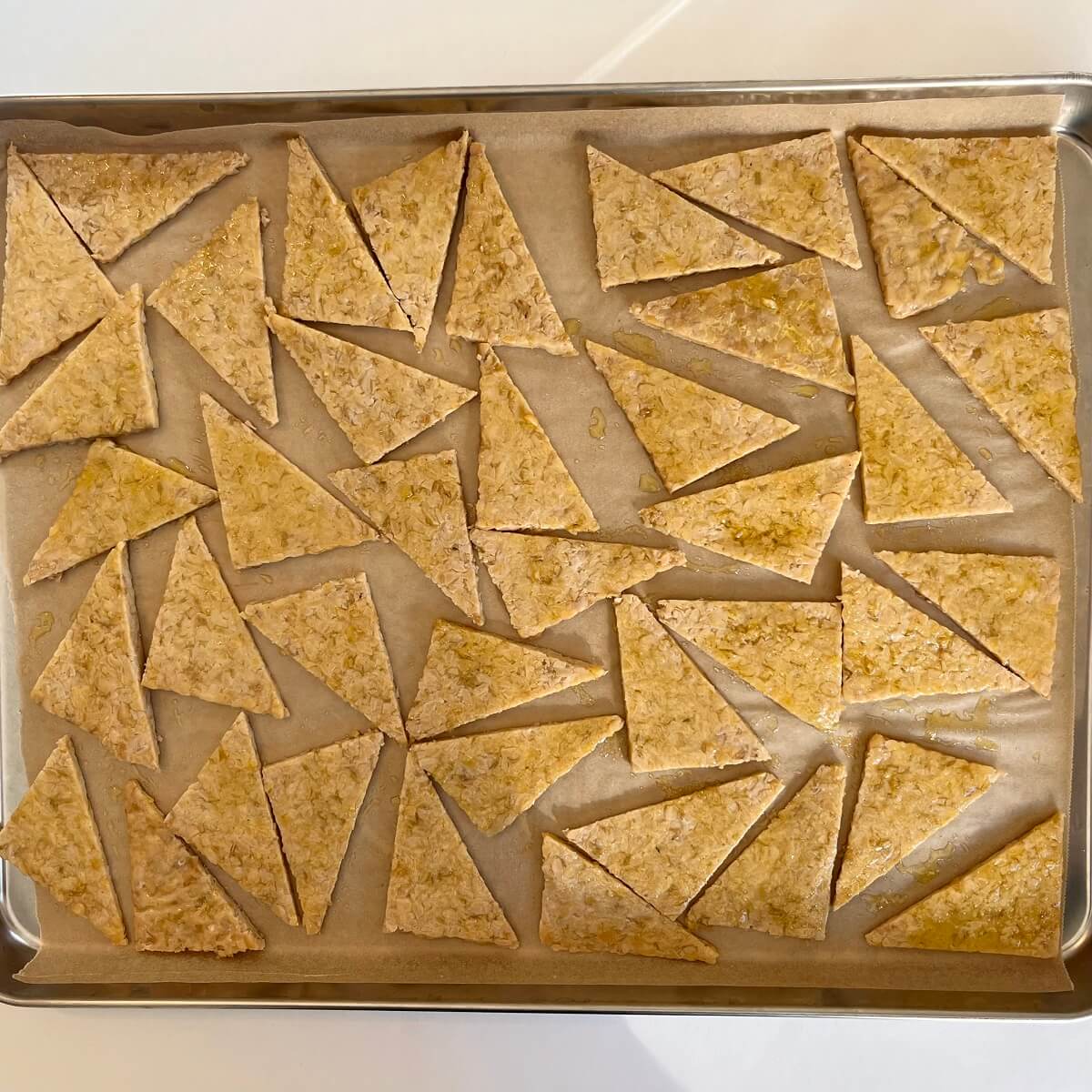 Tempeh pieces basted with oil and spices on a sheet pan lined with parchment paper.