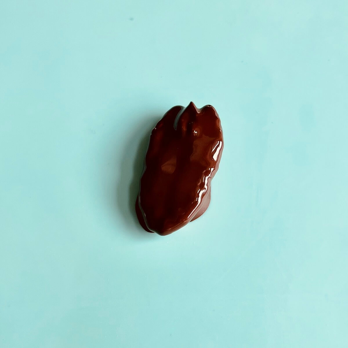 One pecan half covered in wet melted chocolate.