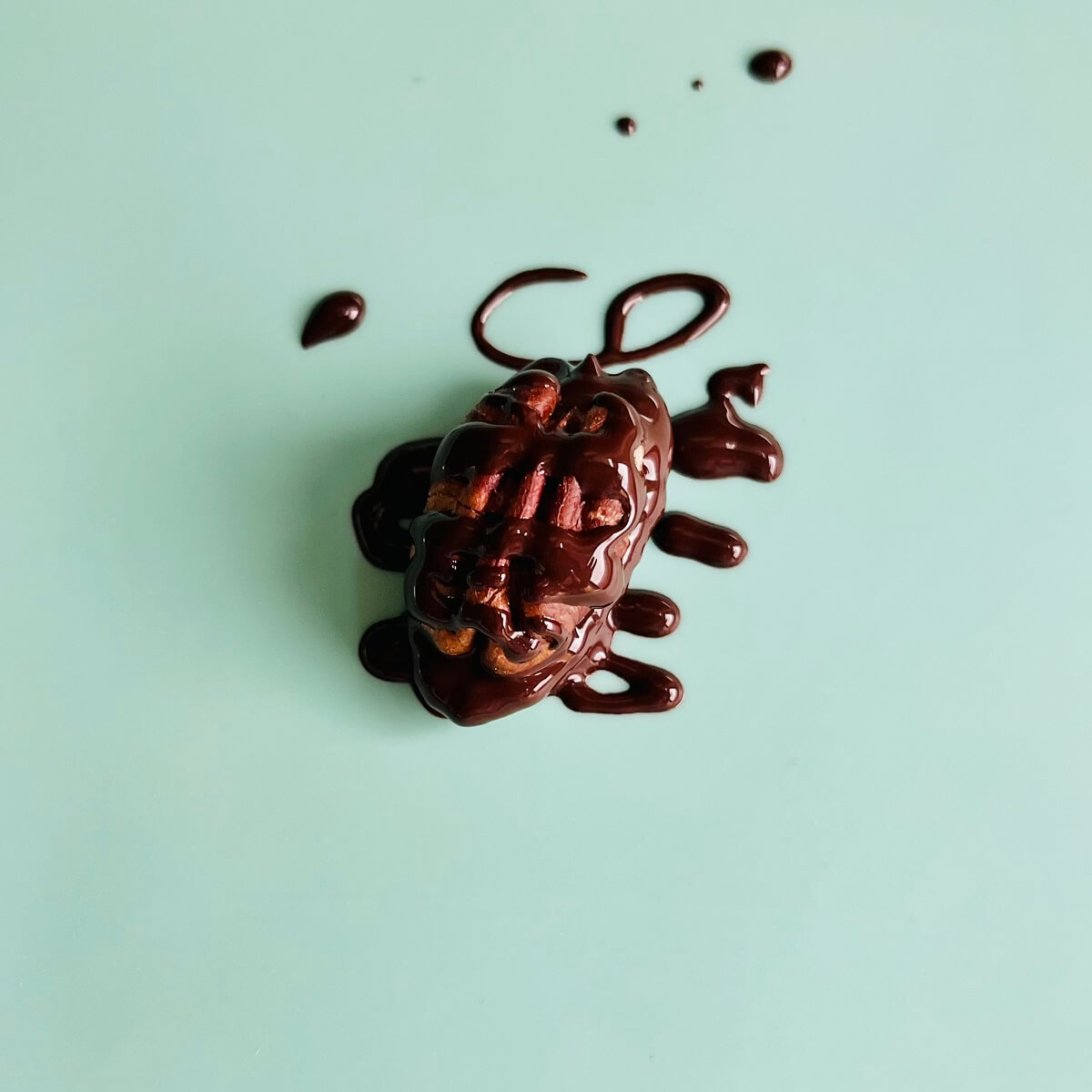 A chocolate drizzled pecan on a turquoise silicone baking mat.