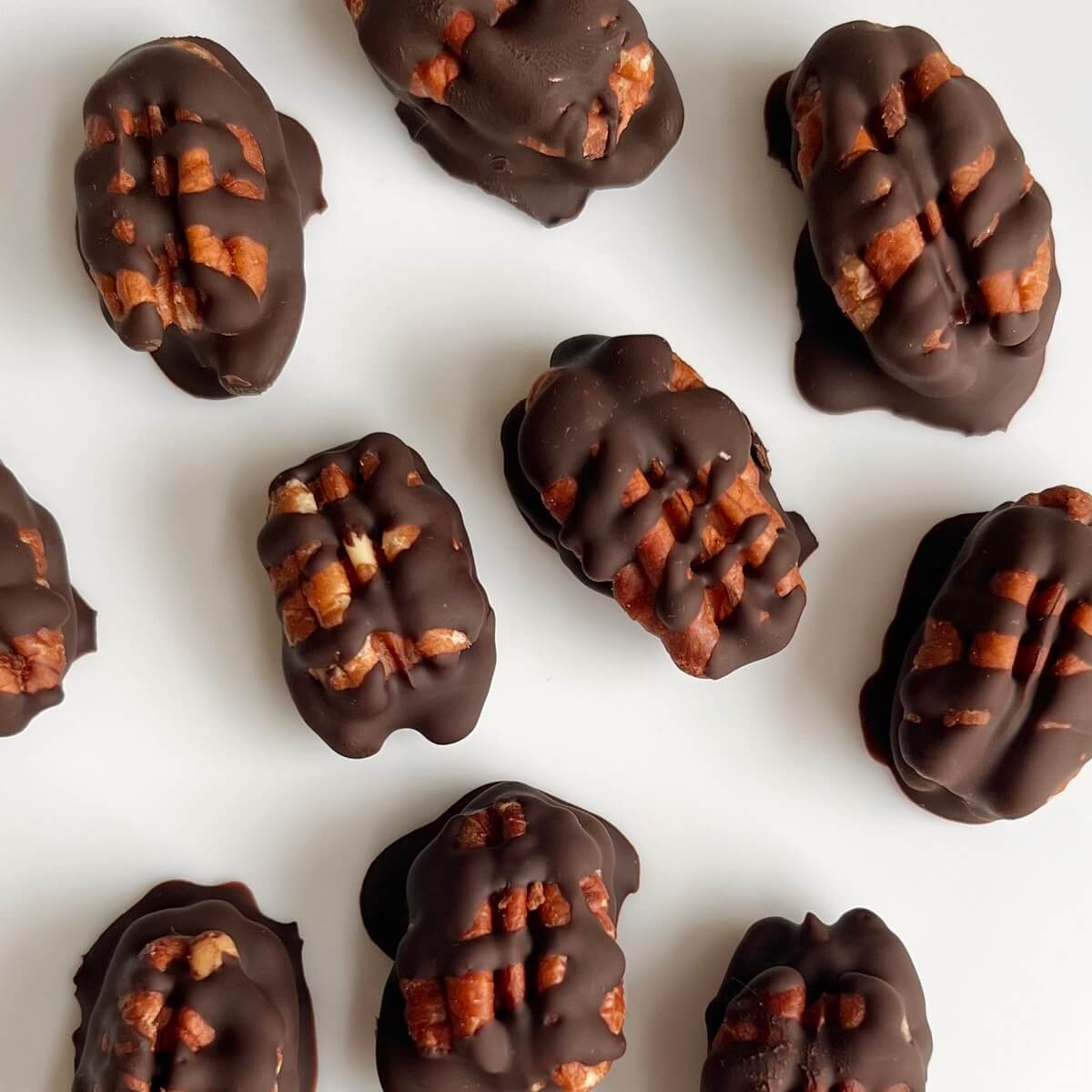 Dark chocolate covered pecans on a white plate.