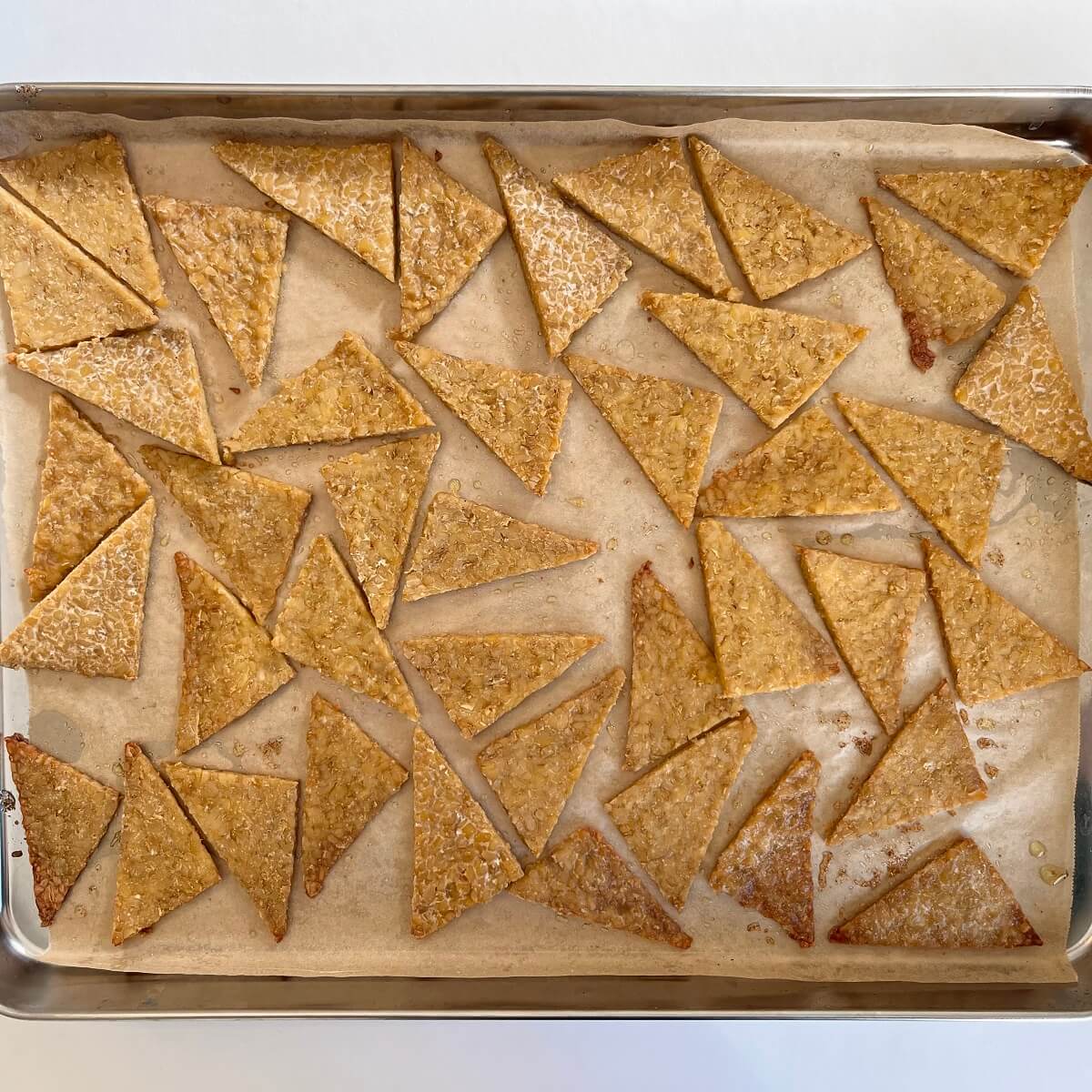 Tempeh pieces on a sheet pan, halfway through the baking process.