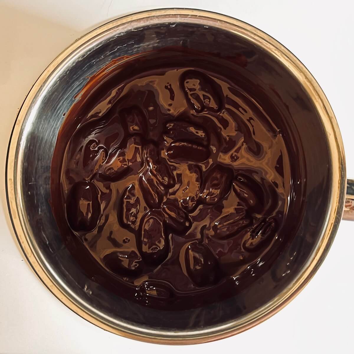 Melted dark chocolate and pecan halves in a metal pot.
