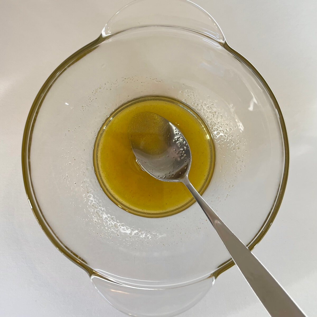 Olive oil and spices in a glass bowl with a spoon.