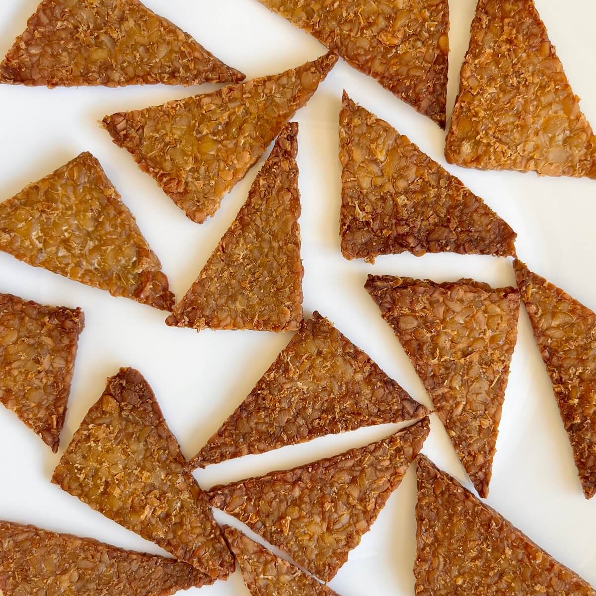 Triangle shaped tempeh chips on a white plate.