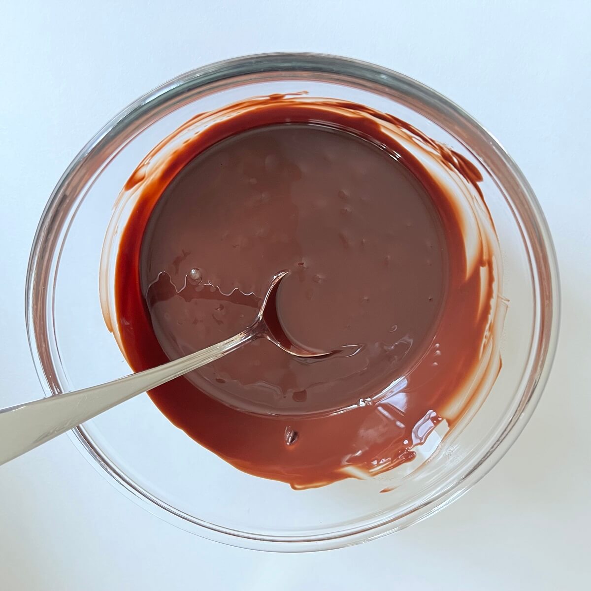 A mixture of melted chocolate, lavender flowers, and olive oil in a glass bowl.